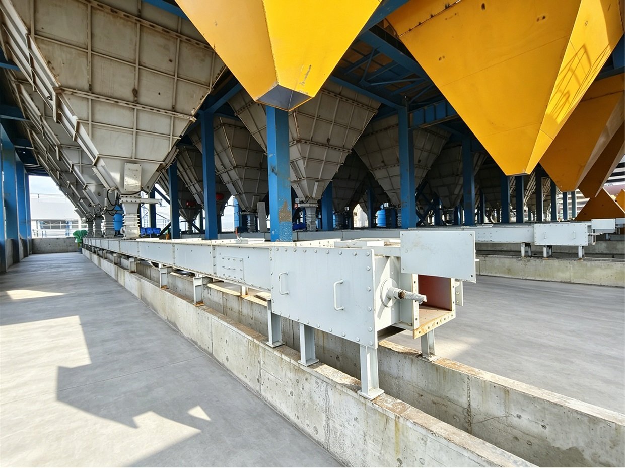 Enclosed en-masse chain conveyor running beneath a row of storage silos with discharge chutes at an alumina project